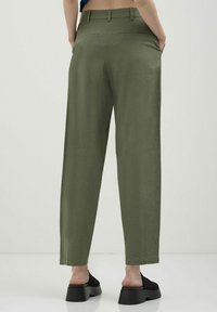 Pantalons larges vert olive en tissu léger avec une texture lisse. Comprend deux poches arrière et une coupe nette et soignée.