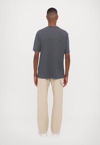 Gray cotton graphic t-shirt with a relaxed fit, featuring text print on the back. Paired with beige cargo pants and white shoes.