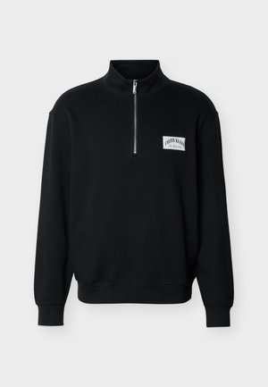 Sort langærmet pullover med kvart-lynlåslukning ved kraven og hvidt logo-mærke med teksten "Calvin Klein New York City" på brystet.