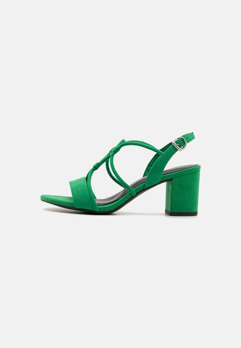 Green suede heeled sandals with a block heel, featuring crisscross straps and an adjustable buckle on the ankle strap.