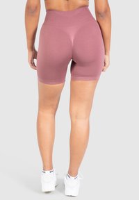 Pantalones cortos deportivos de tiro alto, rosa, con tela texturizada, de longitud a medio muslo, costuras suaves y un diseño ajustado. Llevados con zapatillas blancas.