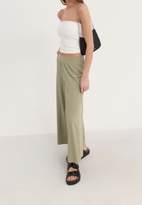 Pantaloni a gamba larga verde chiaro con texture a coste, abbinati a un top bianco aderente senza maniche e sandali platform neri. Inclusa una borsa a tracolla nera.