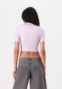 Világoslila cropped top rövid ujjakkal, sima textúrával és fitted kialakítással, magas derekú szürke farmernadrággal párosítva.