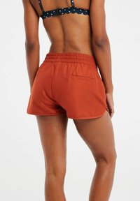 Pantalones cortos de color óxido, ligeros, con una cintura elástica, que cuentan con un bolsillo trasero y una textura suave.