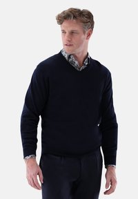  navyfarbener V-Ausschnitt-Pullover aus weichem Stoff, mit langen Ärmeln und einem darunter getragenen Hemd mit Kragen, das ein Blumenmuster zeigt.