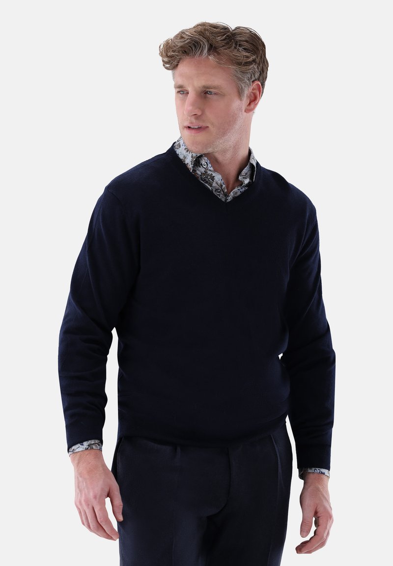 navyfarbener V-Ausschnitt-Pullover aus weichem Stoff, mit langen Ärmeln und einem darunter getragenen Hemd mit Kragen, das ein Blumenmuster zeigt.