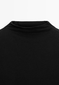 Schwarzer, gerippter Rollkragenpullover mit glatter Textur und figurbetontem Design. Der Kragen ist leicht hochstehend und betont eine klare, minimalistische Silhouette.