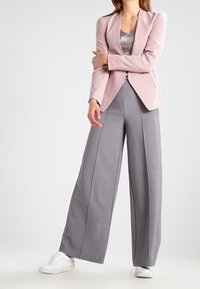 Blazer rose clair ajusté, pantalons larges gris, et baskets blanches. Textures douces et silhouette épurée.