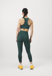 Sutiã desportivo verde com design de costas nadador, leggings de cintura alta combinando e sapatos de atletismo amarelos brilhantes. Tecido suave e elástico com um corte ajustado.