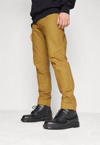 Bruna chinos med slim fit, i kombination med svarta snörboots. Tyget verkar robust; byxorna har sidofickor och en slät yta.