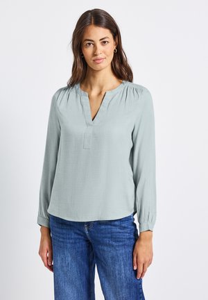 Lichtgrijze blouse met lange mouwen en een V-hals, voorzien van geplooide schouderdetails, gecombineerd met blauwe spijkerbroek. Glad materiaal, casual pasvorm.