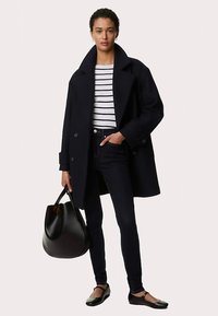 Cappotto di lana blu navy con grandi rever, top a righe bianche e blu navy, jeans scuri, ballerine nere, con una borsa in pelle nera. Design semplice, texture liscia.