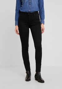 Vaqueros negros de corte ajustado con una textura suave, de cintura alta y diseño de cinco bolsillos, combinados con botas negras de tobillo y una camisa de mezclilla.