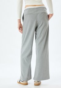 Lichtgrijze wijde broek met een fijne streep patroon, elastische tailleband en zakken. Gecombineerd met casual witte en zwarte schoenen.