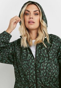 Grön och svart leopardmönstrad jacka med huva, dragkedja fram, elastiska muddar och dragsko i midjan. Lättviktigt tyg med en slät textur.