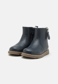 Botines de cuero azul marino con cremallera lateral y forro de piel sintética, que cuentan con una suela de goma beige y detalles de costura mínimos.