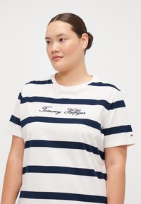 Hvidstribet t-shirt med marineblå vandrette striber, rund halsudskæring, broderet "Tommy Hilfiger"-logo, korte ærmer og mærkedetalje.