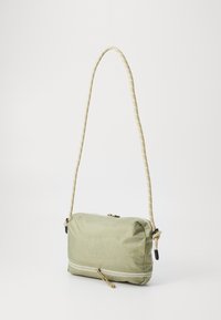 Borsa a tracolla verde in nylon con una superficie liscia, dotata di una tracolla intrecciata e una chiusura a zip con una piccola pull e un dettaglio inferiore a contrasto.