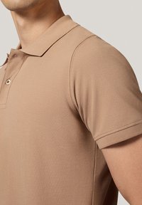 Beżowa koszulka polo z teksturowanej tkaniny, charakteryzująca się klasycznym kołnierzykiem, zapięciem na dwa guziki oraz krótkimi rękawami, eksponująca dopasowany krój.