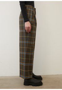 Bruna rutiga byxor med blå och gula accenter, som har hög midja och vida ben, i kombination med svarta kraftiga ankelboots.