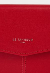 Portafoglio in pelle rossa con finitura texture, caratterizzato dal logo goffrato in argento "LE TANNEUR 1898" e da un design pulito e angolare.