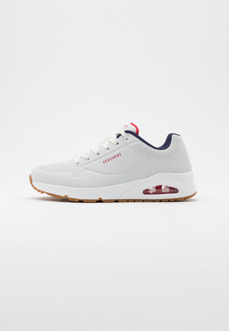 White athletic shoes with a textured upper, navy accents, red logo, and a visible air cushion in the sole. Rubber outsole for traction.