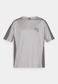 T-shirt d'athlétisme gris clair à manches courtes avec des panneaux gris plus foncés sur les manches et les côtés, présentant un petit graphique abstrait et le texte "Karma" sur la poitrine.