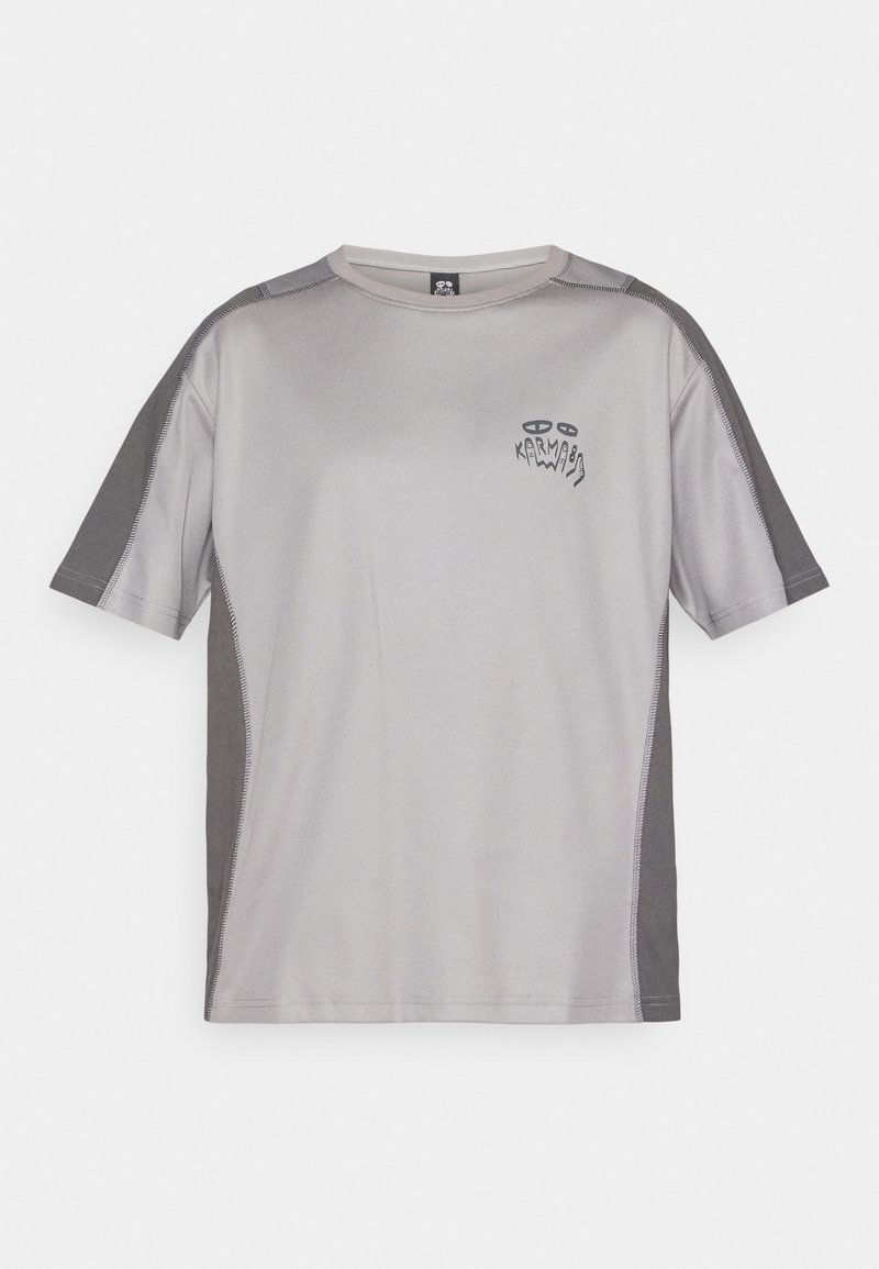 T-shirt d'athlétisme gris clair à manches courtes avec des panneaux gris plus foncés sur les manches et les côtés, présentant un petit graphique abstrait et le texte "Karma" sur la poitrine.