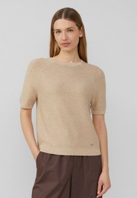 Beiger Strickpullover mit kurzen Ärmeln, rundem Halsausschnitt, strukturiertem Muster und gerippten Säumen. Der Stoff wirkt weich und leicht.