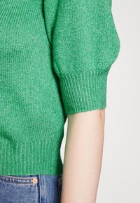 Groene gebreide trui met korte pofmouwen en geribde manchetten. Heeft een textuurstof en een cropped ontwerp, aangevuld met denim onderstukken.