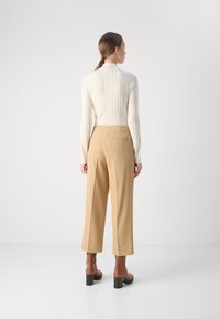 Beige vide benbukser med en struktureret pasform, der har baglommer og en glat tekstur. Kombineret med en let ribbet striktop.