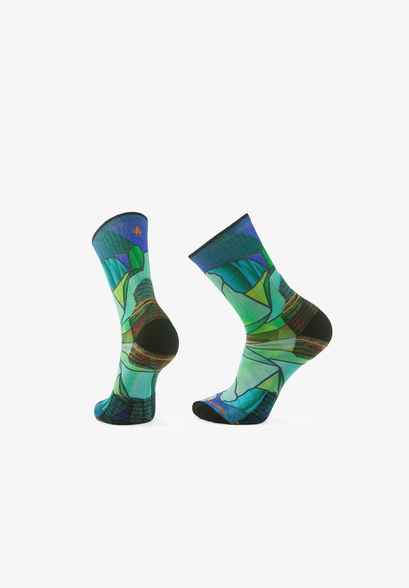 Calzini colorati con motivi geometrici in tonalità di verde e blu, caratterizzati da una texture a coste e dettagli neri sul bordo e sulla punta.