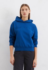 Felpa con cappuccio blu realizzata in tessuto morbido, con un logo testurizzato "Marc O'Polo" sul davanti, e polsini e orlo rilassati.