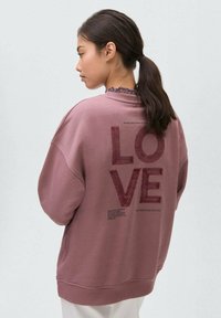 Veľká, fialová mikina s textom "LOVE" v textúrovanej vínovej farbe. Má rebrovaný výstrih a manžety, mäkkú tkaninu a spustené plecia.