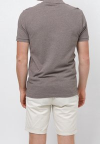 Polo marron à manches courtes avec une texture douce, doté d'un col discret et d'un ourlet légèrement incurvé, associé à un short blanc retroussé.