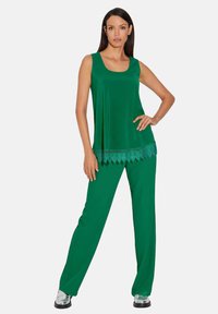 Grünes ärmelloses Top mit Spitzenbesatz am Saum, kombiniert mit passenden, weit geschnittenen Hosen. Glatter Stoff, lockere Passform und leichter Glanz.