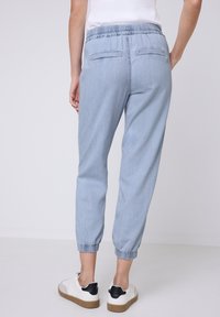 Pantalones casuales de color azul claro con cinturilla elástica, puños elásticos y dos bolsillos traseros. Llevados con zapatillas blancas y negras.