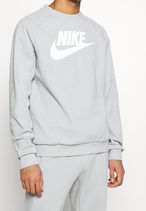 Mężczyzna w jasnoszarej bluzie Nike i pasujących spodniach, z wyraźnie widocznym logo Nike na klatce piersiowej.