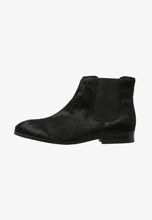 Bottine Chelsea noire jusqu'à la cheville avec talon bas, bout pointu, panneau latéral élastique et tige à texture lisse.