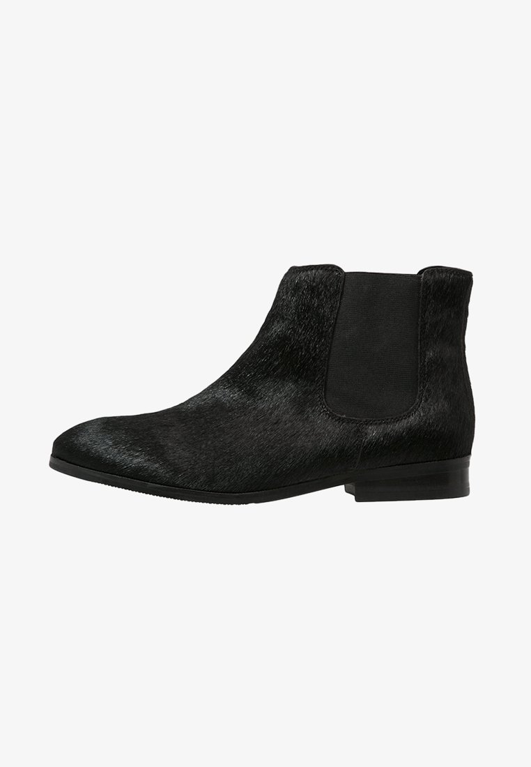 Bottine Chelsea noire jusqu'à la cheville avec talon bas, bout pointu, panneau latéral élastique et tige à texture lisse.