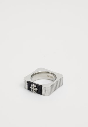 Square silver metal ring with black textured detail and a small silver decorative emblem, branded "GUESS" inside.