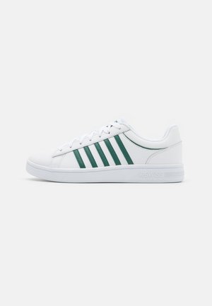 Weiße Sneaker mit grünen Streifen, Obermaterial aus synthetischem Material, flache Sohle, runde Zehenform und Schnürsystem. Mit Logo an der Ferse.