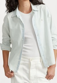 Ljust blå skjorta med knappar och uppvikt ärm, tillverkad av mjukt tyg, med en liten logga på bröstet och en avslappnad passform.