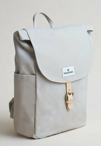 Zaino in canvas grigio chiaro con patta pieghevole, fibbia in pelle e tasca frontale. Presenta una maniglia superiore e spallacci regolabili.