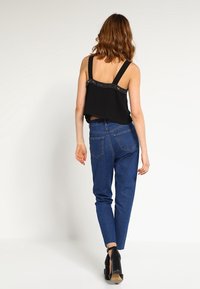 Top corto nero con cuciture decorative sul colletto, abbinato a jeans blu a vita alta e stivaletti neri alla caviglia.