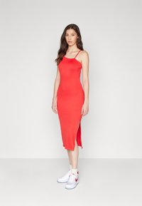 Robe midi rouge sans manches avec fentes latérales, texture lisse. Associée à des baskets blanches avec des accents rouges et des chaussettes.