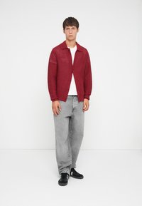 Red knit cardigan with a collared neckline, layered over a white t-shirt, paired with loose gray jeans and black sneakers.