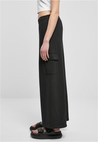 Černé kalhoty širokého střihu vyrobené z jemné látky, s boční kapsou a elastickým pasem. Spárovány s černými sandály.