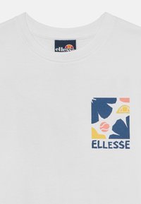 Balta kokvilnas T-krekls ar krāsainu ģeometrisku logotipa druku zilā, dzeltenā, rozā un sarkanā krāsā. Apaļš kakls un īsas piedurknes.