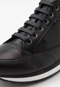 Svart lädersneaker med rund tå, strukturerad ovandel, tonade skosnören, metallöga och kontrasterande vit mellansula.